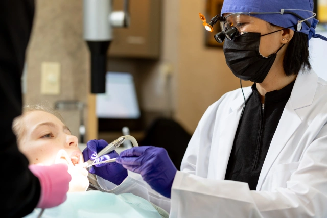 Dentist in protective gear examining patient's teeth in dental clinic setting.