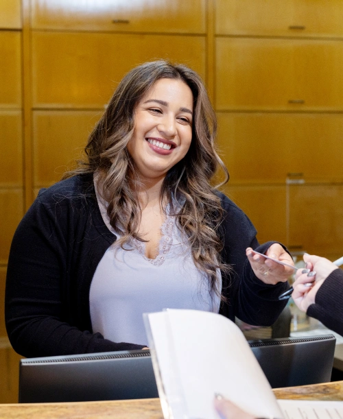 Woman smiling at dental reception desk with paperwork in professional office setting.